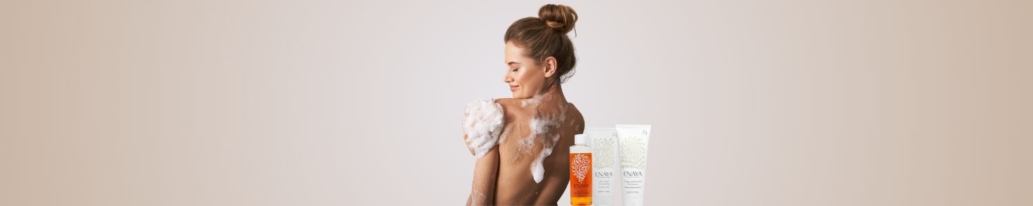 Banni&egrave;re soins du corps ENAYA, femme de dos prenant une douche moussante sur fond nude avec des produits de douche Enaya align&eacute;s &agrave; droite.